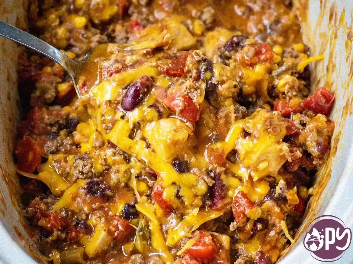 Slow Cooker Cowboy Casserole with melted cheese, beans, corn, and peppers in a rustic crockpot.